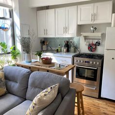 a kitchen and living room are shown with white cabinets, wood floors, and gray couches