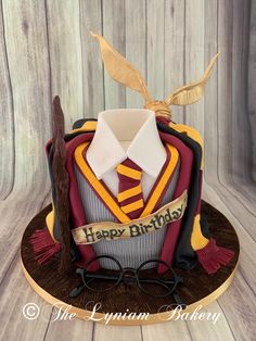 a harry potter birthday cake with glasses, tie and hat on it's stand