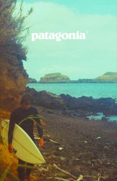 a man holding a surfboard on top of a rocky beach