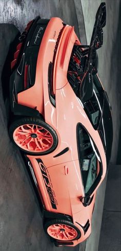 an orange sports car parked in a parking lot next to a cement wall with red rims