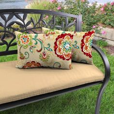 two pillows sitting on top of a metal bench in the grass next to flowers and water