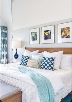 a bed with white sheets and blue pillows in a bedroom next to pictures on the wall