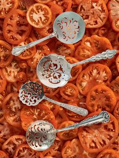 three spoons and two forks are laying on top of sliced tomatoes