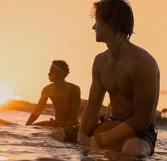 two men are sitting on surfboards in the water at sunset, one man is looking off into the distance