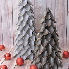 two metal christmas trees with red balls on the ground next to them and one is made out of tin