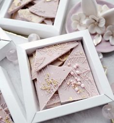 three white boxes with pink and gold decorated cookies in them on top of a table