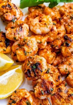 grilled shrimp with lemon wedges and basil on a white plate next to a slice of lemon