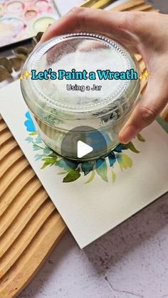 someone is painting a vase with flowers and leaves on the paper next to some crafting supplies