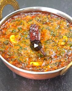 a metal pot filled with food sitting on top of a black counter next to a wooden spoon