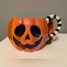 an orange pumpkin mug with black and white stripes around it's face, decorated like a jack - o - lantern