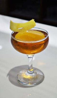 a glass filled with liquid sitting on top of a white table next to a slice of lemon