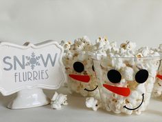 three plastic cups filled with popcorn sitting on top of a white table next to a sign that says snow flurries