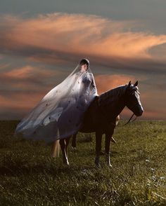 a bride riding on the back of a horse in a field at sunset with her veil flowing