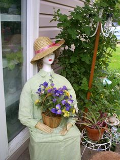 a mannequin wearing a hat and holding a basket of flowers in front of a house