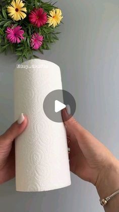 a person holding a roll of toilet paper in front of a flower arrangement on the wall