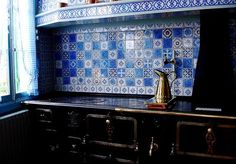 a kitchen with blue and white tiles on the wall, stove top and countertop