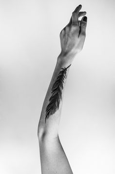 black and white photograph of a person's arm with a feather tattoo on it