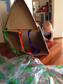 a baby playing with a cardboard boat on the floor