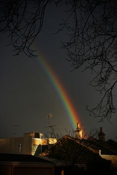 a rainbow shines brightly in the dark sky above some houses and trees on a gloomy night