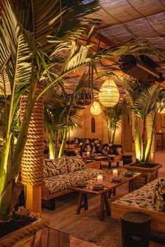 a room with couches, tables and palm trees in the center is lit by candles