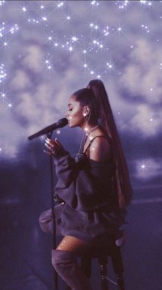 a woman sitting on top of a stool holding a microphone in front of her face