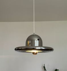 a silver light hanging from the ceiling in a room with white walls and potted plants