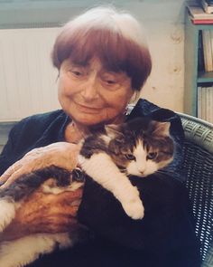 an older woman holding two cats in her arms