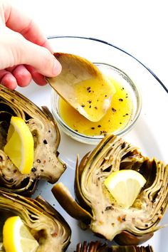 a plate with artichokes on it and someone dipping something into the bowl