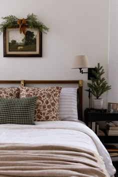 a bed with pillows and blankets on top of it next to a painting hanging above the headboard