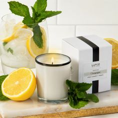 the candle is next to some lemons and mint leaves on a tray with a box