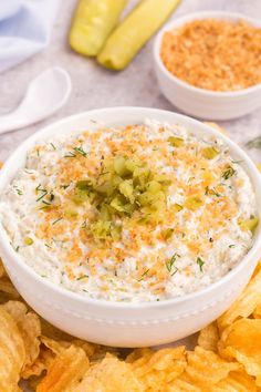 a white bowl filled with dip surrounded by chips and pickle slices on the side