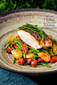 a plate with some fish and potatoes on it, next to a blue cloth in the background