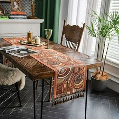 a dining room table covered with an orange and brown paisley print cloth next to a fireplace