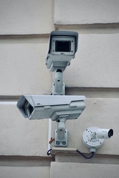 two security cameras mounted on the side of a building next to a wall with a camera attached