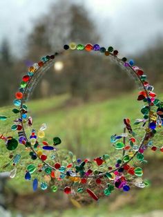 a circular sculpture made out of glass beads and other colorful objects in front of a grassy field