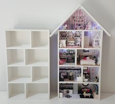 a doll house is shown next to a bookcase with dolls in it and lights on the shelves