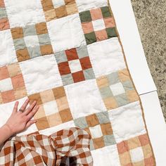 a person laying on the ground next to a large patchwork quilt with their hand resting on it