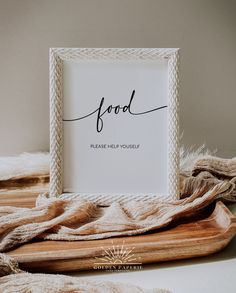 a wooden tray topped with a white framed sign next to a pile of brown blankets