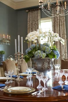 a dining room table set with place settings and flowers in a vase on the centerpiece