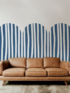 a brown leather couch sitting in front of a wall with blue and white stripes on it