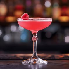 a pink cocktail with a raspberry garnish in a coupe glass on a bar