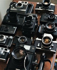 many old cameras sitting on top of a wooden table next to each other, all with different lens types