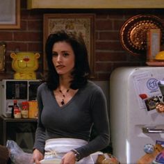 a woman standing in front of a refrigerator with food on the counter next to it