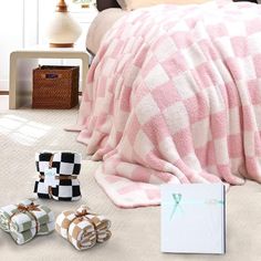 a bed covered in pink and white checkered blanket next to baby's shoes