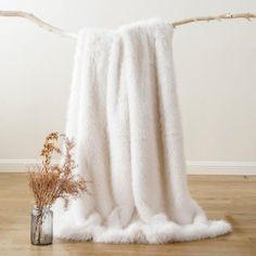 a white throw blanket sitting on top of a wooden floor next to a vase with dried flowers