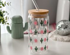 a glass jar with pink flowers and cactus on it