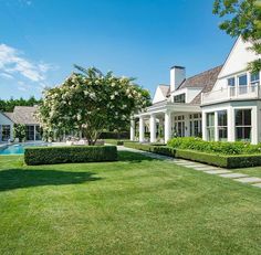 a large white house sitting next to a lush green field with trees and bushes in front of it