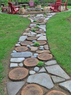 a stone path made out of logs in the middle of a grassy area with chairs around it