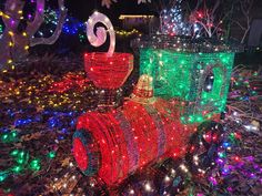 a train covered in christmas lights sitting on top of a pile of grass next to trees