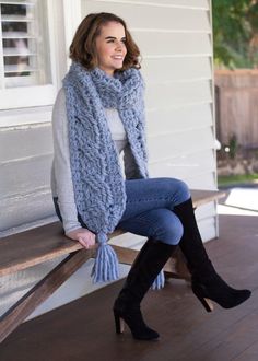 a woman sitting on a bench wearing boots and a scarf